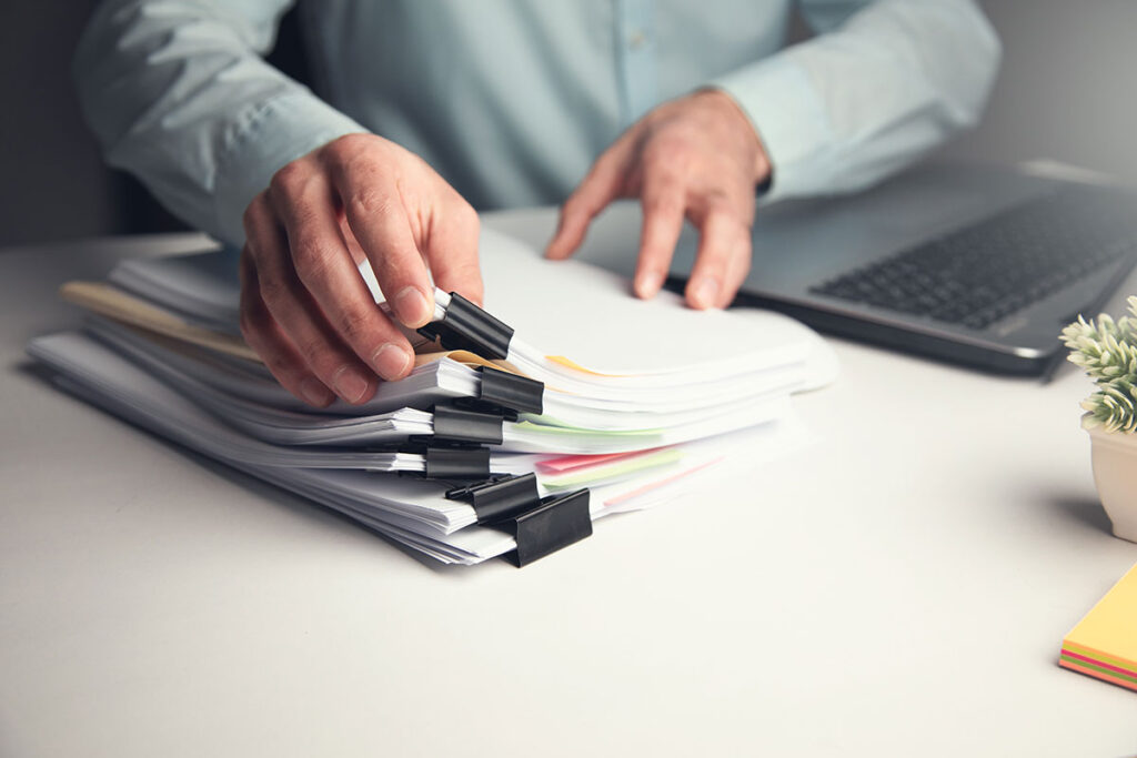 man going through stacks of papers working on laptop